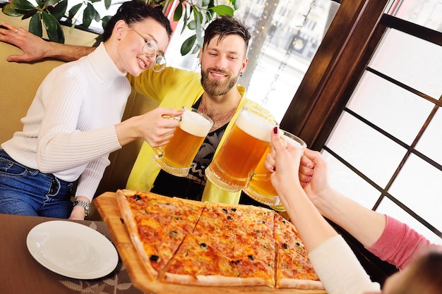 Grupo de amigos comiendo pizza y bebiendo cerveza en el bar o en la cafetería