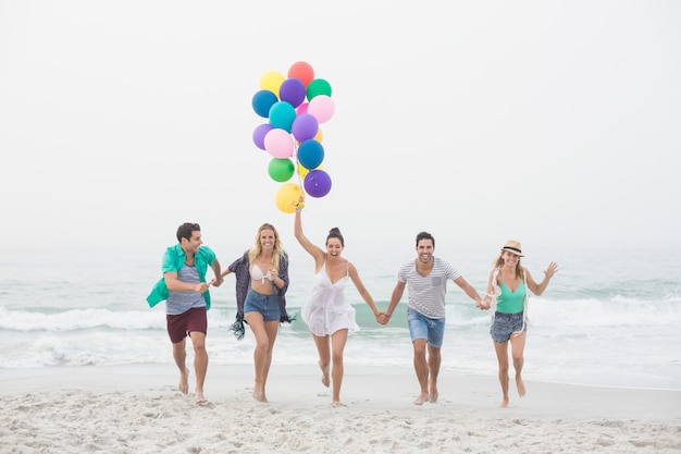 Grupo de amigos corriendo en la playa con globos