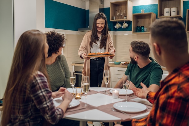 Grupo de amigos disfrutando de la cena sentados juntos en la mesa de la cocina