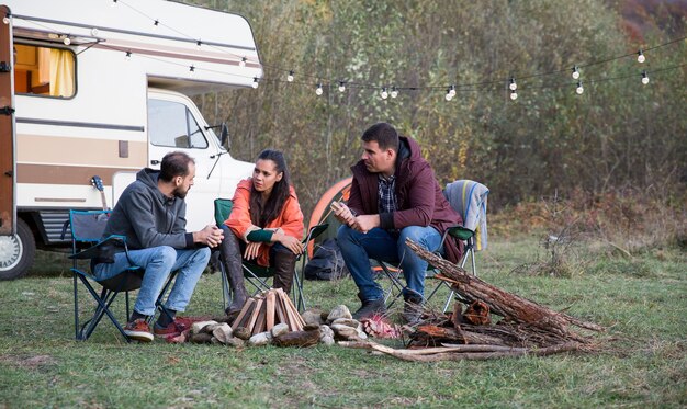 Foto grupo de amigos disfrutando de su tiempo juntos en las montañas acampando con autocaravana retro.