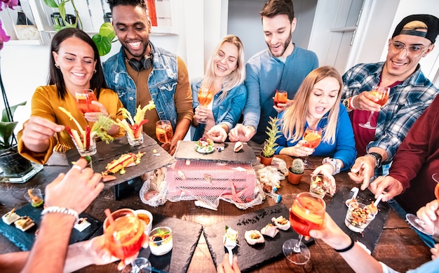 Grupo de amigos divirtiéndose en la cena previa al buffet bebiendo cócteles spritz y comiendo bocadillos