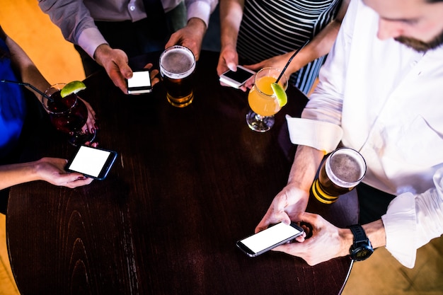 Grupo de amigos enviando mensajes de texto y tomando una copa en un bar