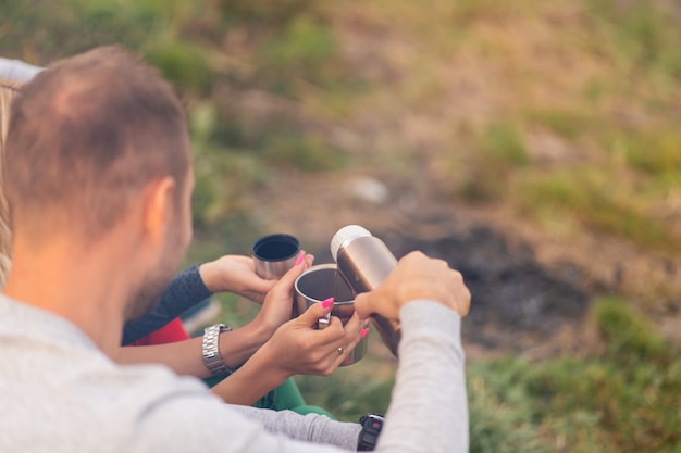 Un grupo de amigos está disfrutando de una bebida caliente de un termo, en una tarde fresca junto a un incendio en el bosque. Tiempo divertido para acampar con amigos