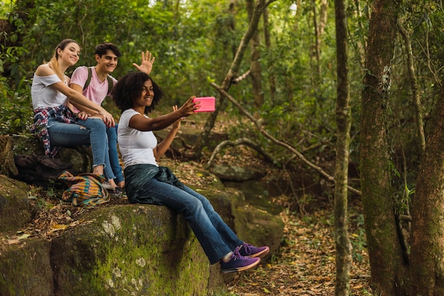 Grupo de amigos excursionistas sentados en una roca toman un selfie