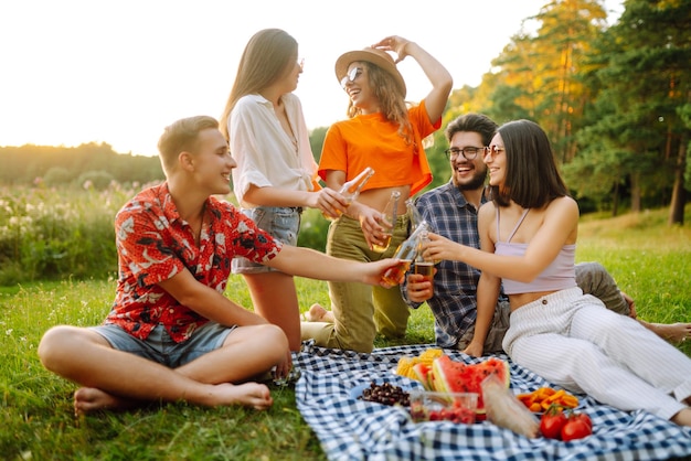 Grupo de amigos felices animados bebiendo cervezas en el parque de verano concepto de amistad o fiesta