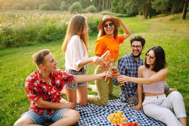 Grupo de amigos felices aplausos beben cervezas en el parque de verano Amistad o concepto de vacaciones