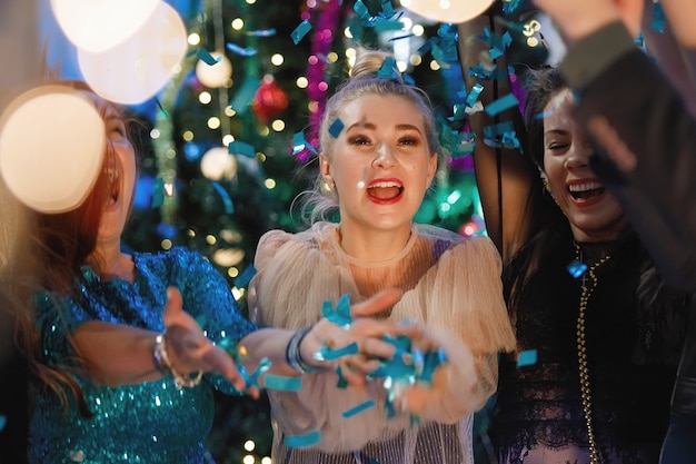 Grupo de amigos felices bailando cerca del árbol de Navidad. Las mujeres se ríen, se regocijan.