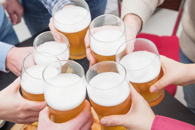 Grupo de amigos felices bebiendo y brindando cerveza en casa