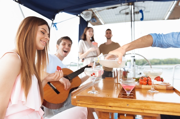 Grupo de amigos felices bebiendo cócteles de vodka en fiesta en barco al aire libre, verano