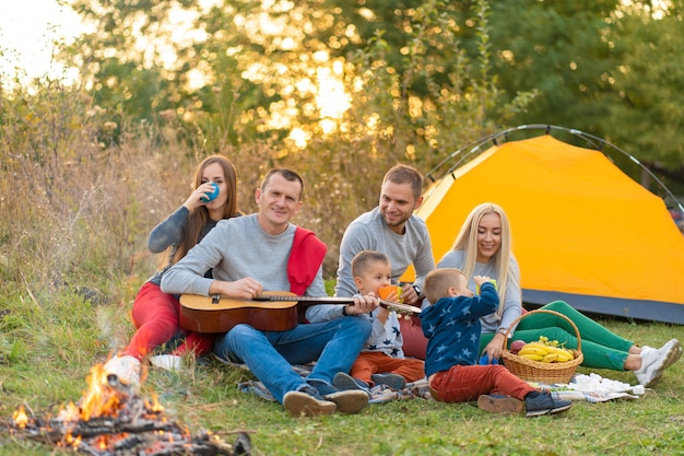 Grupo de amigos felices con carpa y bebidas tocando la guitarra en el camping