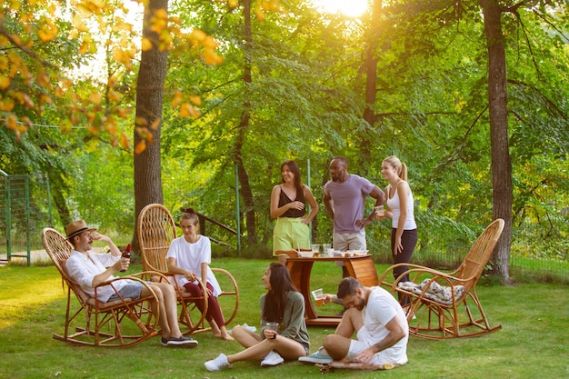 Grupo de amigos felices comiendo y bebiendo cervezas en la cena de barbacoa al atardecer