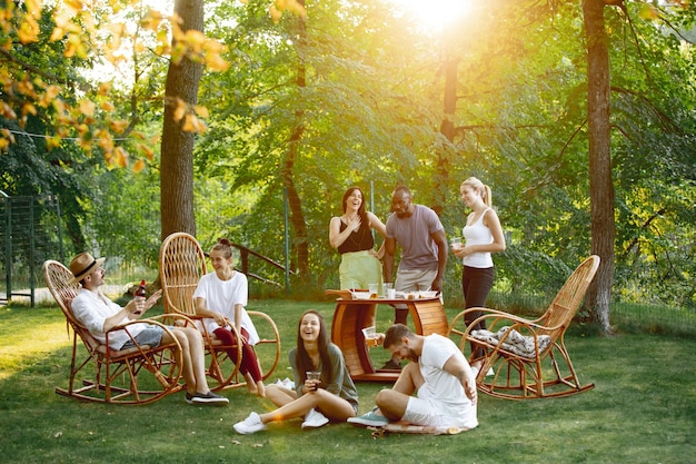 Grupo de amigos felices comiendo y bebiendo cervezas en la cena de barbacoa al atardecer