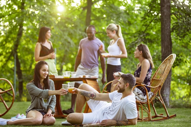 Grupo de amigos felices comiendo y bebiendo cervezas en la cena de barbacoa al atardecer