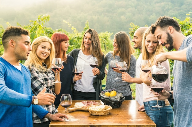 Grupo de amigos felices divirtiéndose al aire libre bebiendo vino tinto