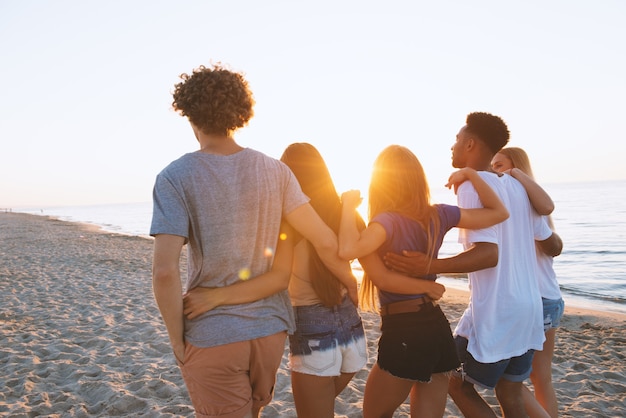 Grupo de amigos felices divirtiéndose en la playa al amanecer