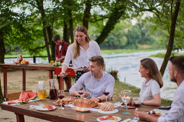grupo de amigos felices haciendo un picnic en una cena francesa al aire libre durante las vacaciones de verano cerca del río en la hermosa naturaleza