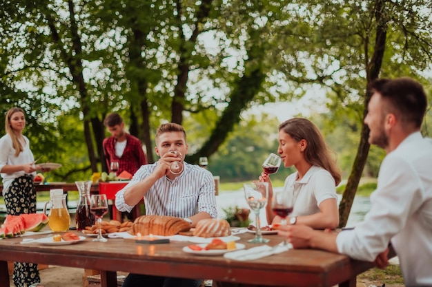 Grupo de amigos felices que tienen un picnic en una cena francesa al aire libre durante las vacaciones de verano cerca del río en la hermosa naturaleza.