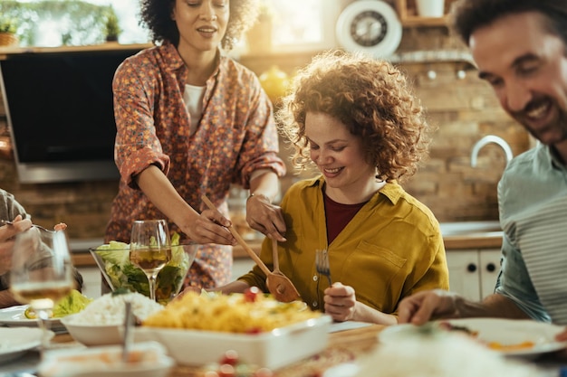 Grupo de amigos felices reunidos para almorzar en la mesa del comedor. El foco está en la mujer pelirroja.