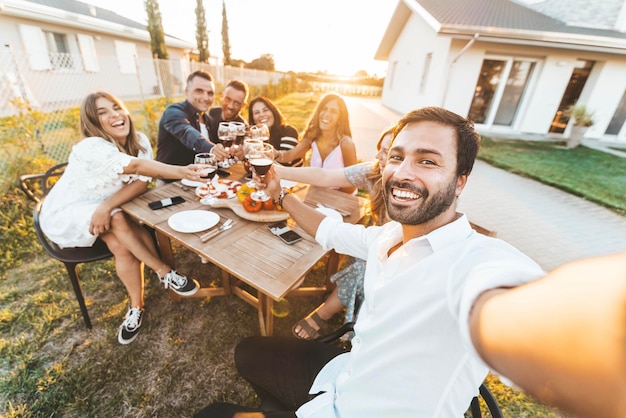 Grupo de amigos felices tomando selfie en una cena al aire libre con barbacoa en el jardín de su casa