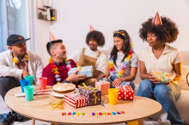 Grupo de amigos en una fiesta de cumpleaños en el sofá de casa sonriendo entregando regalos