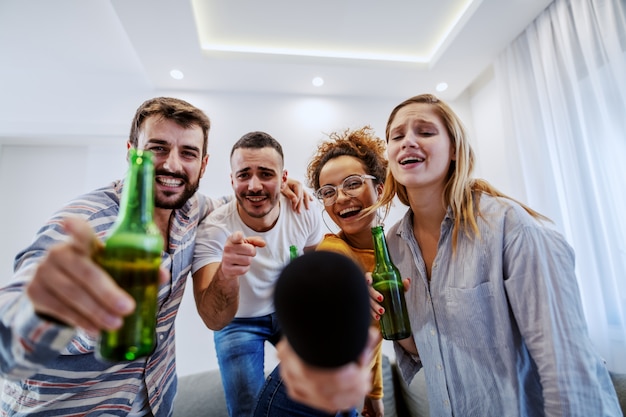 Foto grupo de amigos con fiesta de karaoke en casa. todos apuntan a la cámara.