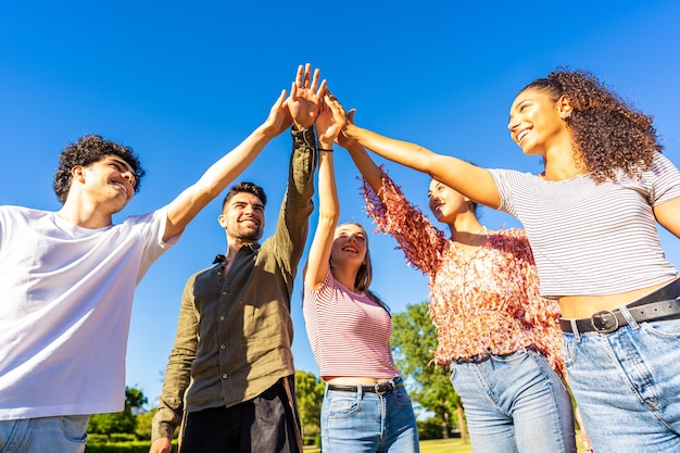 Grupo de amigos de la generación z felices tocando la mano levantada el uno al otro. Concepto de confianza en el futuro y éxito en la vida. Diversos estudiantes multiétnicos milenarios que se unen al aire libre en la naturaleza del parque de la ciudad