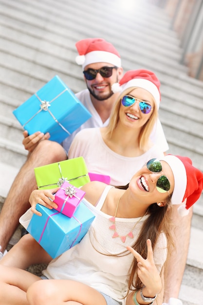 Grupo de amigos con gorro de Papá Noel sentado en la ciudad con regalos