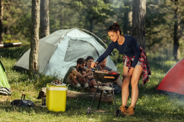 Grupo de amigos haciendo barbacoa mientras acampan en el bosque