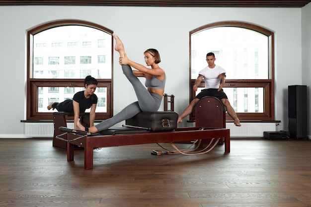 Grupo de amigos haciendo ejercicios de glúteos arrodillados de pilates en camas reformadoras en un gimnasio en un concepto de salud y fitness