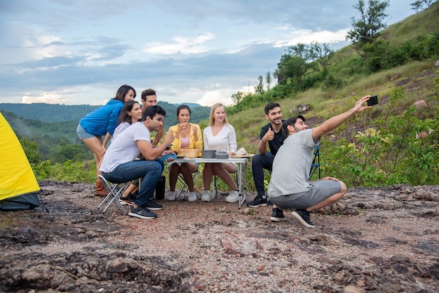 Un grupo de amigos, hombres y mujeres, preparan una mesa de picnic para cocinar en medio de hermosas montañas y selfies