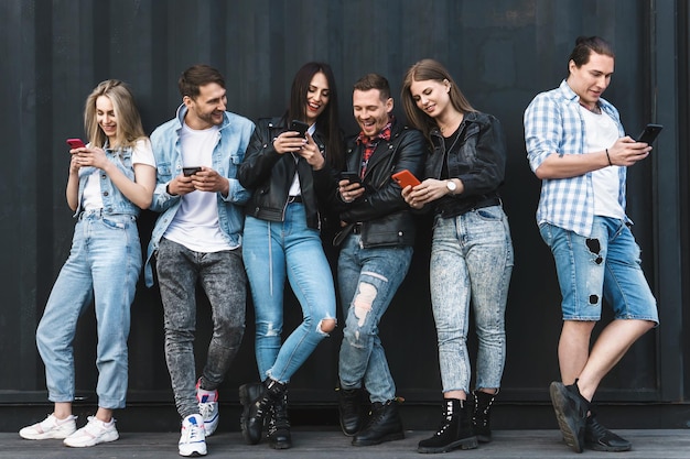 Grupo de amigos jóvenes y elegantes que usan teléfonos inteligentes para enviar mensajes en lugar de una comunicación real