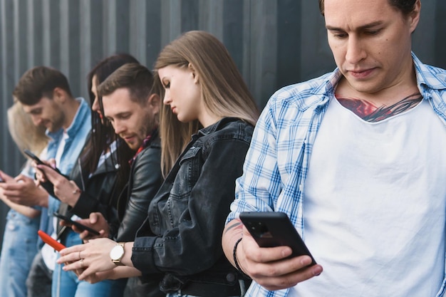 Grupo de amigos jóvenes y elegantes que usan teléfonos inteligentes para enviar mensajes en lugar de una comunicación real