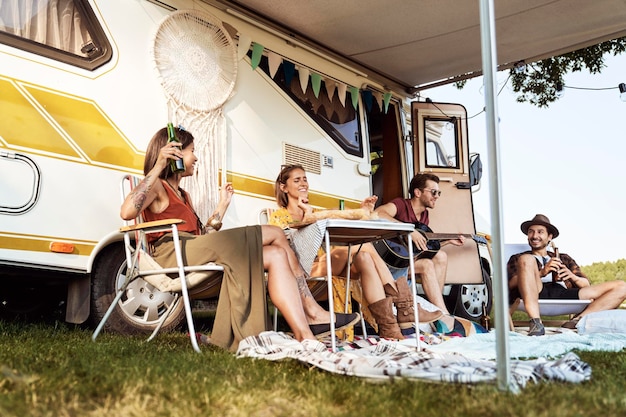 Grupo de amigos jóvenes pasando tiempo en el lado del camper con música de guitarra