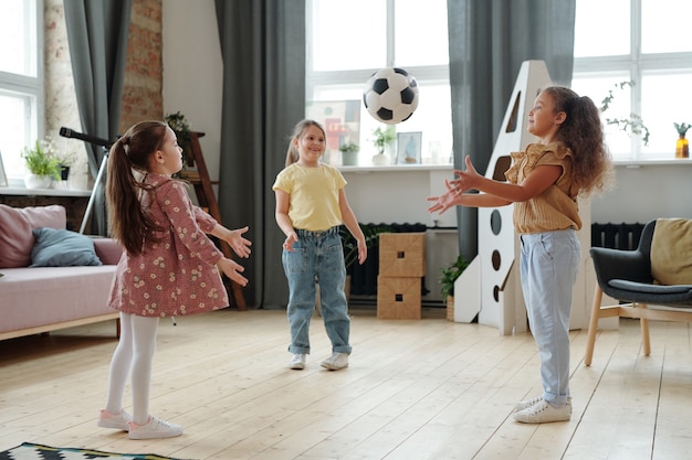 Grupo de amigos jugando a la pelota juntos mientras está de pie en la habitación en casa