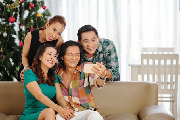 Grupo de amigos maduros jouful posando para selfie en árbol Cheistmas en casa