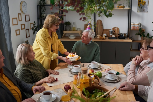 Grupo de amigos mayores celebrando un cumpleaños con pastel juntos en la mesa en casa