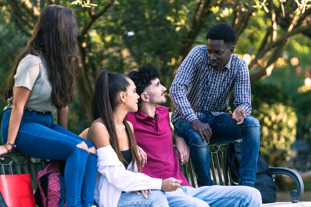 Grupo de amigos multiculturales sentados en un banco de un parque mientras habla