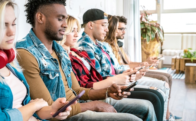 Grupo de amigos multirracial en un momento aburrido usando un teléfono inteligente móvil - Enfoque selectivo