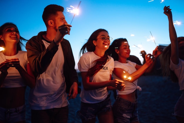 Grupo de amigos en la noche en la playa con bengalas Jóvenes amigos disfrutando de unas vacaciones en la playa