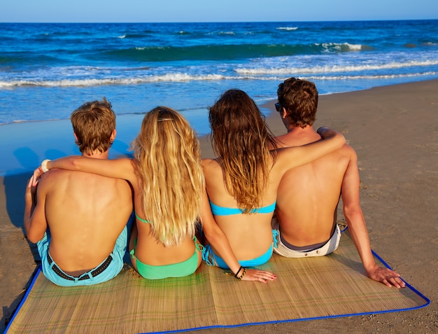 Grupo de amigos parejas sentadas en la playa de arena trasera