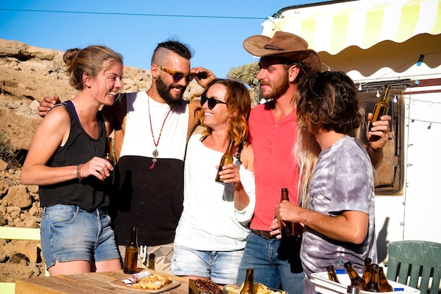 Grupo de amigos de personas alternativas disfrutando y celebrando al aire libre en el campo rural con botellas de cerveza y risas