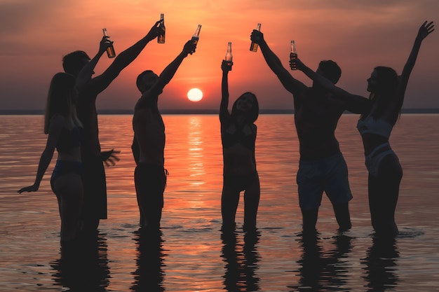 El grupo de amigos de pie en el agua y gritando contra la puesta de sol.