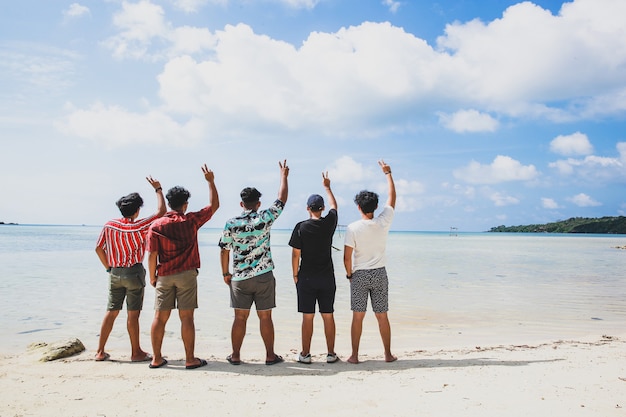 Grupo de amigos de pie y levantando la mano juntos disfrutando de la vista de la playa tropical durante las vacaciones de verano