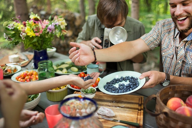 Un grupo de amigos reunidos en una mesa al aire libre compartiendo platos de frutas frescas y ensaladas