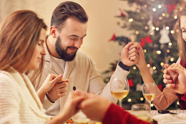 Grupo de amigos rezando sobre la mesa de Navidad