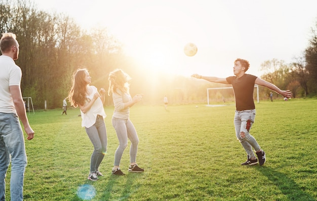 Un grupo de amigos en ropa casual juega fútbol al aire libre. La gente se divierte y se divierte. Descanso activo y pintoresco atardecer.