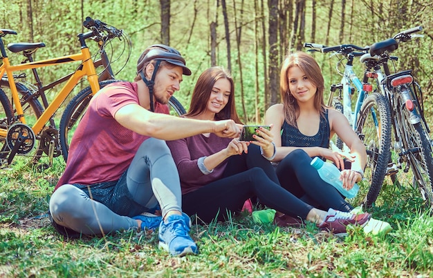 Foto un grupo de amigos está sentado en el suelo, relájese y hable después de andar en bicicleta en el parque. concepto de amistad.