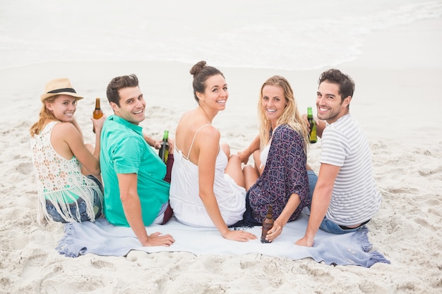 Grupo de amigos sentados uno al lado del otro en la playa con botellas de cerveza