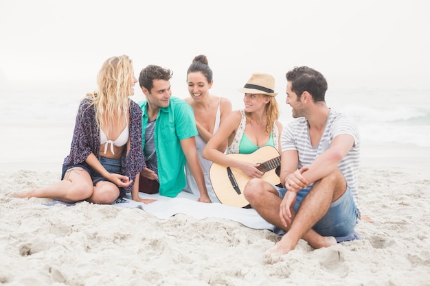 Grupo de amigos sentados en la playa con guitarra