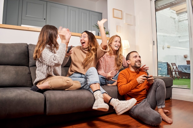 Grupo de amigos sentados en el sofá en la sala de estar y jugar videojuegos en casa